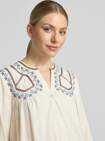 Frauenmodel trägt Bluse aus Viskose-Mix mit kurzer Knopfleiste Modell 'IRISA' von b.young, cremefarbener Stoff, blaue Stickerei, Nahaufnahme Oberkörper. Damen Bluse, Regular Fit, Serafino-Ausschnitt, Rückenlänge 62 cm, Ärmellänge 63 cm.