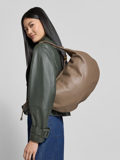 Frauenmodel trägt Shoulder Bag mit Logo-Print Modell 'Thess' von Coccinelle in Braun, Struktur mit Reißverschluss, Ganzkörperansicht Rückansicht. Hauptfach mit Reißverschluss, Tunnelzug-Trageriemen, Maße ca. 40x31x6 cm, Schulterriemen ca. 50 cm.