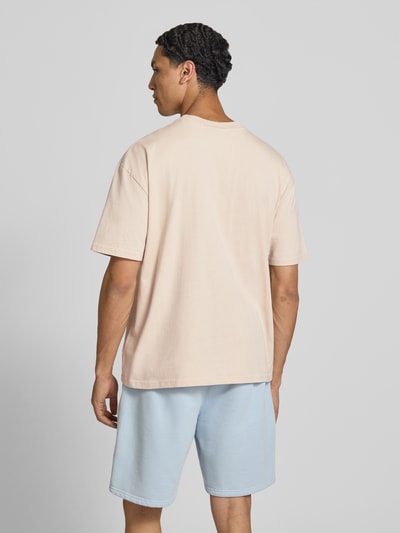 Männermodel trägt Oversized T-Shirt mit Label-Stitching von Pegador aus Baumwoll-Mix in Beige mit Rundhalsausschnitt, Rückenlänge 70 cm, Ganzkörperansicht Rückansicht.