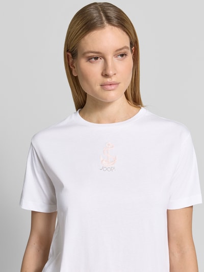 Frauenmodel trägt T-Shirt mit Rundhalsausschnitt und Stitching Modell 'Tino' von JOOP! aus reiner Baumwolle in Weiß, Nahaufnahme Oberkörper.