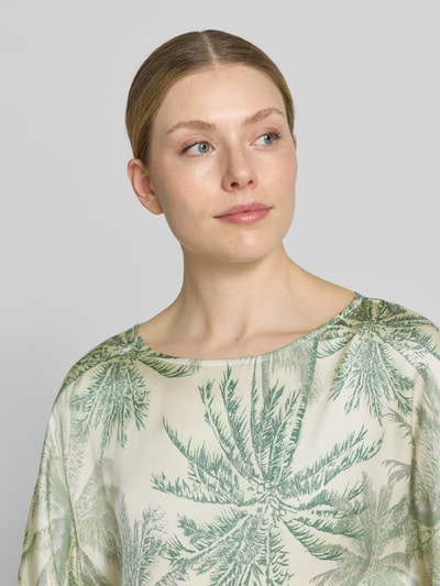 Frauenmodel trägt Relaxed Fit Kurzarmbluse aus reiner Viskose von s.Oliver BLACK LABEL mit grünem Palmblattmuster auf Creme, Nahaufnahme Oberkörper.