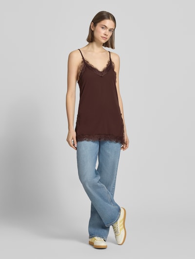 Frauenmodel trägt Regular Fit Top mit Spitzenbesatz von Gina Tricot in Dunkelbraun, V-Ausschnitt, verstellbare Spaghetti-Träger, Ganzkörperansicht von vorne.