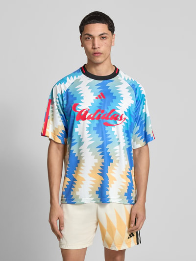 Männermodel trägt Regular Fit T-Shirt mit Allover-Muster von adidas Sportswear, Rundhals, Kurzarm, Label-Print, bunte Zickzack-Optik, Ganzkörperansicht von vorne.