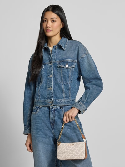 Frauenmodel trägt Shoulder Bag mit Logo-Applikation Modell 'Jet Set' von MICHAEL Michael Kors mit Allover-Logo-Print, Nahaufnahme Oberkörper.