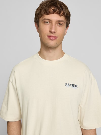 Männermodel trägt T-Shirt mit Label-Detail von REVIEW in Creme, Reine Baumwolle, Lockerer-Schnitt, Rundhalsausschnitt, 1/2-Arm, Nahaufnahme Oberkörper.
