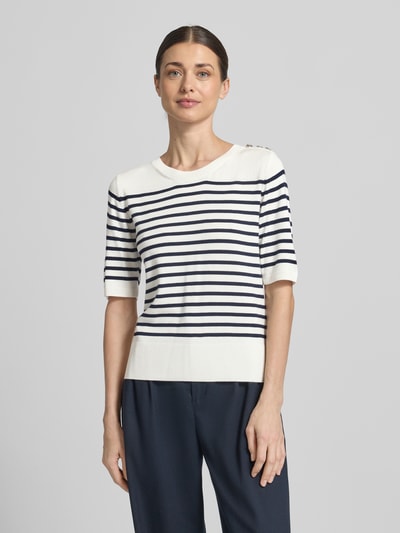 Frauenmodel trägt Strickshirt aus Viskose-Elasthan-Mix mit Knopfleiste von Milano Italy, weiß-dunkelblau gestreift, Ganzkörperansicht von vorne.