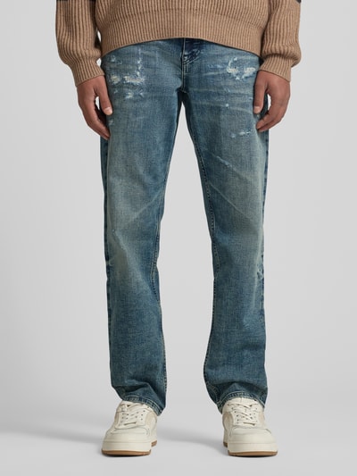 Männermodel trägt Tapered-Fit Jeans aus Baumwoll-Mix Modell 'TROY' von BOSS Orange in blauer Denim-Optik mit Destroyed-Details, Label-Patch, Nieten, 5-Pocket-Design, Knopf und verdecktem Reißverschluss, Ganzkörperansicht von vorne.