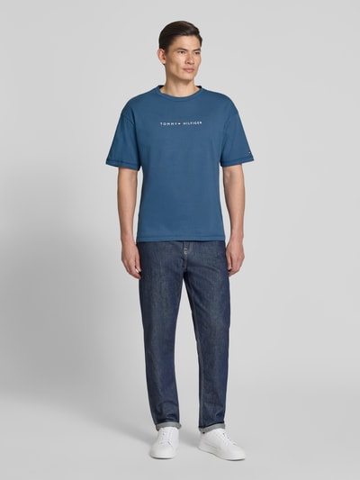 Männermodel trägt Regular Fit T-Shirt mit Label-Schriftzug aus reiner Baumwolle von Tommy Hilfiger, unifarben, Ganzkörperansicht von vorne.