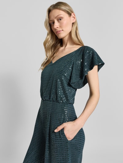 Modelka kobieca ma na sobie 'Schimmernder Jumpsuit mit V-Ausschnitt' od Vera Mont, ciemnozielony, materiał z połyskiem, krój regular fit, dekolt V, zamek z tyłu, długość pleców w rozmiarze 36: 149 cm, szerokość w rozmiarze 36: 33 cm, długość rękawa w rozmiarze 36: 17 cm, długość całkowita: 153 cm, długość nogawki: 83 cm, tekstura z drobnymi cekinami, widok na górną część ciała z przodu