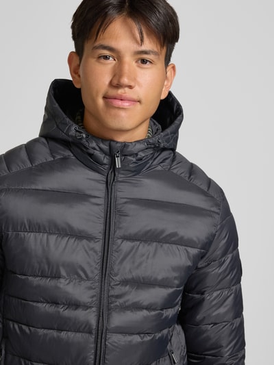 Męski model nosi Regular Fit kurtkę z efektem pikowania Model 'KINGSLEY' od JACK & JONES, kolor czarny, kaptur, zamek błyskawiczny, wpuszczane kieszenie, Długość tyłu w rozmiarze M: 70 cm, Szerokość ramion w rozmiarze M: 45 cm, Szerokość klatki piersiowej w rozmiarze M: 52 cm, Długość rękawów w rozmiarze M: 67 cm, zbliżenie na górną część ciała, przód