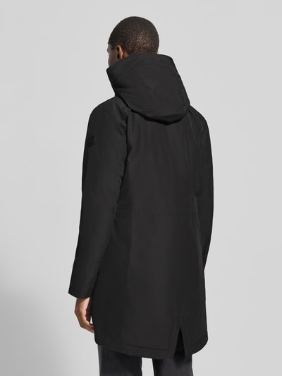 Vrouwenmodel draagt zwarte Regular Fit Parka met capuchon Model 'Alana' van Didriksons, steekzakken, ruglengte maat 36: 90 cm, schouderbreedte 38 cm, borstwijdte 48 cm, mouwlengte 74 cm, ganzebody aanzicht achteraan.