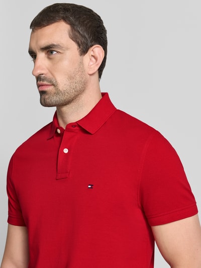 Mężczyzna nosi Regular Fit Poloshirt aus Baumwoll-Mix von Tommy Hilfiger w intensywnie czerwonym kolorze, gładka tekstura, zbliżenie na górę ciała, kontekst: Herren Poloshirt von Tommy Hilfiger