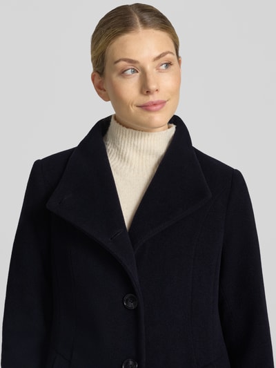 Vrouwenmodel draagt Regular fit lange jas met opstaande kraag model 'NADA' van Milo Coats, materiaalmix met scheerwol, knoopsluiting, steekzakken, ruglengte maat 36: 118 cm, schouderbreedte 40 cm, borstwijdte 47 cm, mouwlengte 67 cm, donkere kleur, zachte textuur, Nahaufnahme Oberkörper.