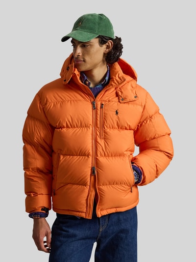Männermodel trägt Steppjacke mit Zweiwege-Reißverschluss von POLO RALPH LAUREN in Orange, Kapuze mit Tunnelzug, Ganzkörperansicht von vorne.