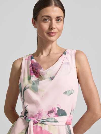 Frauenmodel trägt Knielanges Cocktailkleid mit Bindegürtel von Vera Mont aus Chiffon, Taillierter Schnitt, Wasserfall-Ausschnitt, florales Muster, Nahaufnahme Oberkörper. Brustweite Größe 36: 40 cm, Rückenlänge: 104 cm.
