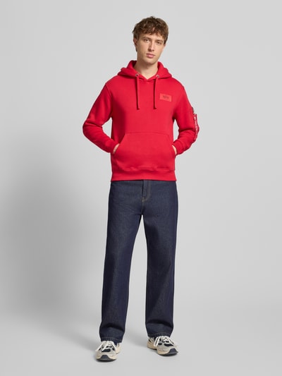 Männermodel trägt Hoodie mit Känguru-Tasche von Alpha Industries in Rot, Baumwoll-Mix, Regular-Fit, Label-Patch, Ganzkörperansicht von vorne.