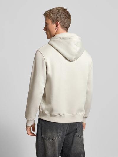 Männermodel trägt Hoodie mit Logo und Känguru-Tasche von Alpha Industries aus Baumwoll-Mix, Regular Fit, dezentes Beige, Ganzkörperansicht Rückansicht.