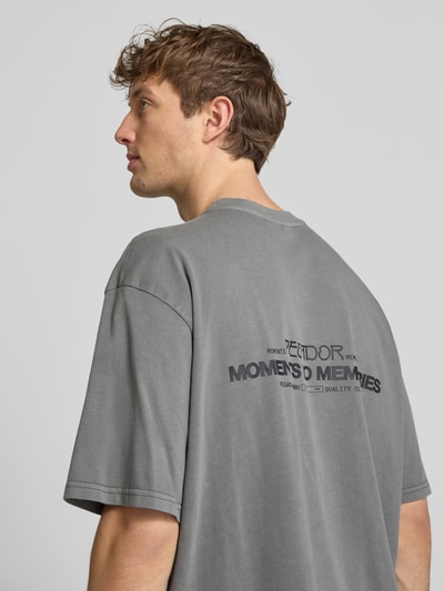 Männermodel trägt Oversized T-Shirt aus Baumwolle Modell 'Hattem' von Pegador in Grau mit Label-Detail, Oversized-Fit, Rückenlänge 70 cm, Reine Baumwolle, Rundhalsausschnitt, Nahaufnahme Oberkörper Rückansicht.