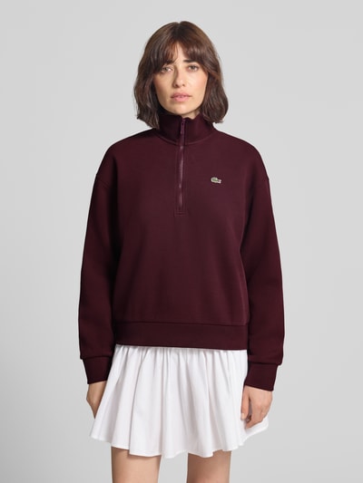 Frauenmodel trägt Relaxed Fit Sweatshirt aus Baumwoll-Mix von Lacoste in Dunkelrot mit Reißverschluss, glatter Textur, Ganzkörperansicht von vorne. Damen Sweatshirt von Lacoste.