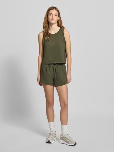 Frauenmodel trägt PUMA x HYROX - Shorts mit Label-Print von PUMA, lockerer Schnitt, olivgrün, elastischer Bund mit Tunnelzug, Ganzkörperansicht von vorne.