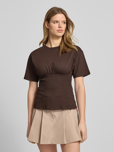 Frauenmodel trägt tailliertes T-Shirt mit Rundhalsausschnitt Modell 'EVELYN' von JJXX aus reiner Baumwolle, Smok-Details, Ganzkörperansicht von vorne.