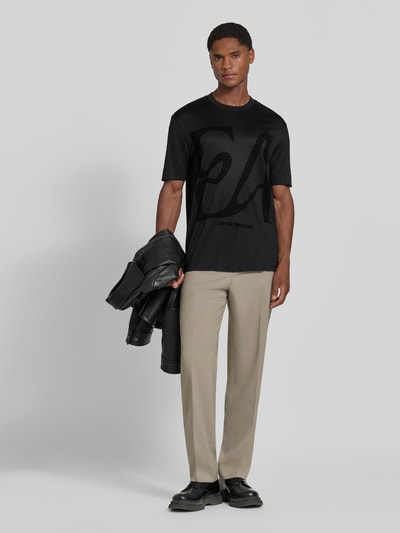 Männermodel trägt T-Shirt mit Label-Print von Emporio Armani in Schwarz, glatte Textur, Lyocell-Baumwoll-Mix, gerade Passform, Ganzkörperansicht von vorne.