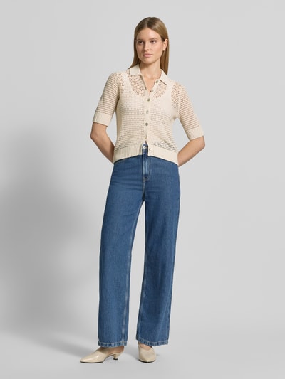 Modelka kobieca ma na sobie Strickjacke aus Leinen mit 1/2-Arm od Christian Berg Woman, jasny beż, krój slim fit, kołnierzyk polo, długa listwa guzikowa, rękaw 1/2, długość tyłu 59 cm w rozmiarze S, długość rękawa 34 cm w rozmiarze S, tekstura ażurowa, przód pełny, zdjęcie całej sylwetki z przodu.