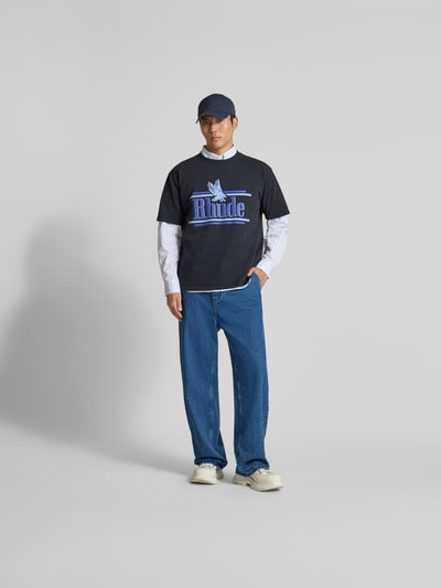 Männermodel trägt Regular Fit T-Shirt aus reiner Baumwolle von RHUDE mit Label-Print, Rundhalsausschnitt, kurzärmelig, blaue Akzente, Herren T-Shirt, Rückenlänge bei Größe M 70 cm, Ganzkörperansicht von vorne.