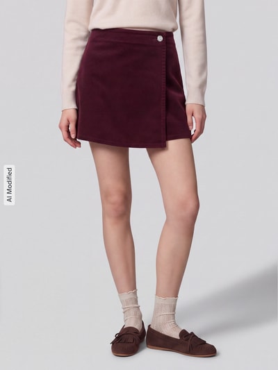 Frauenmodel trägt Regular Fit Short-Rock aus Baumwoll-Mix Modell 'ZEVA' von ONLY in Bordeaux, Cord, Zierknopf, Wickel-Detail, Nahaufnahme Unterkörper, KI-modifiziertes Bild.