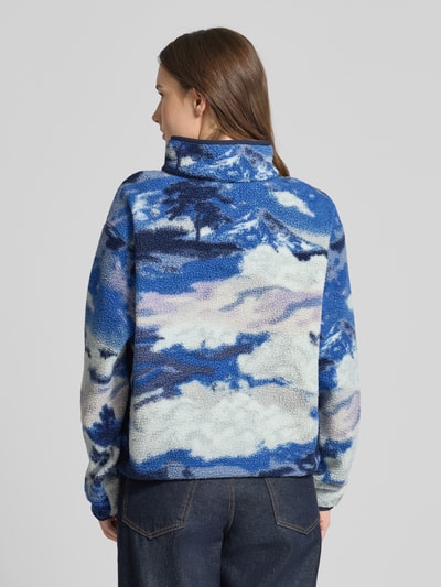 Frauenmodel trägt Regular Fit Pullover mit Logo-Patch Modell 'Helvetia' von COLUMBIA in Fleece-Optik mit Wolkenmuster, Ganzkörperansicht Rückansicht.
