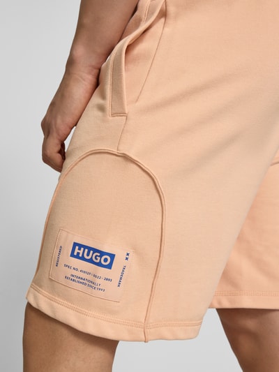 Männermodel trägt Regular Fit Sweatshorts aus Baumwoll-Mix Modell 'NURAZORT' von Hugo Blue in Unifarbe mit Label Patch und Seitentaschen, Nahaufnahme Oberschenkel.