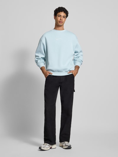 Männermodel trägt Sweatshirt mit Label-Stitching von KARL KANI in Hellblau, Baumwoll-Mix, Lockerer Schnitt, gerippte Abschlüsse, Rundhalsausschnitt, Ganzkörperansicht von vorne.