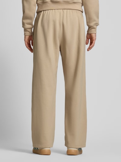 Mężczyzna nosi Wide Fit Sweatpants mit elastischem Bund od adidas Originals, beżowy kolor, bawełniany miks, szeroki krój, widok całej sylwetki z tyłu.