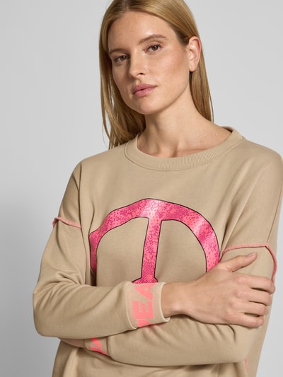 Kobiece modelka nosi Oversized Sweatshirt mit gerippten Abschlüssen od miss goodlife z czystej bawełny, krój oversized, prążkowane wykończenia, okrągły dekolt, nadruk z motywem, beżowy i różowy, tekstura gładka; zbliżenie na górną część ciała