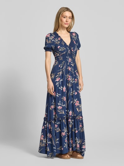 Modelka kobieca ma na sobie Maxikleid aus Viskose mit V-Ausschnitt od Apricot, granatowa sukienka w kwiaty, talia elastyczna, A-linia, długość tyłu w rozmiarze S: 133 cm, szerokość w rozmiarze S: 25 cm, długość rękawa w rozmiarze S: 22 cm, widok całej sylwetki z przodu.
