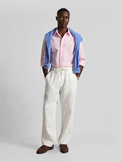 Männermodel trägt Regular Fit Freizeithemd aus reiner Baumwolle von Polo Ralph Lauren in Rosa, kombiniert mit heller Hose, Ganzkörperansicht von vorne.