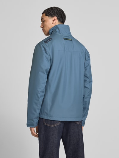 Męski model nosi Midlayer Jacke mit Stehkragen Modell 'CREW' od Helly Hansen, prosty krój, gładka faktura, kolor niebieski, długość tyłu 74 cm, szerokość w rozmiarze M 52 cm, szerokość ramion 49 cm, długość rękawów 68 cm, naszywka z logo, zamek błyskawiczny, tylna perspektywa całej sylwetki.