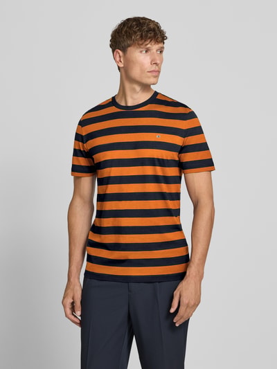 Männermodel trägt Regular Fit T-Shirt mit Logo-Stitching von Christian Berg Men, orange-schwarz gestreift, Reine Baumwolle, Rundhalsausschnitt, Rückenlänge 70 cm bei Größe M, Ganzkörperansicht von vorne.