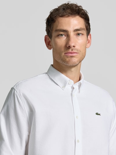 Männermodel trägt weißes Regular Fit Freizeithemd aus reiner Baumwolle von Lacoste, glatte Textur, Nahaufnahme Oberkörper.
