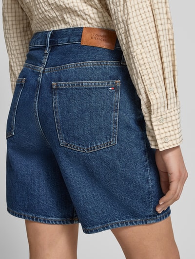 Frauenmodel trägt Straight Leg Bermudas aus reiner Baumwolle Modell 'EMI' von Tommy Hilfiger in Denim-Optik, 5-Pocket-Design, Label-Patch und Logo-Applikation, Regular-Fit, blaue Farbe, grobe Baumwoll-Textur, Ganzkörperansicht Rückansicht.