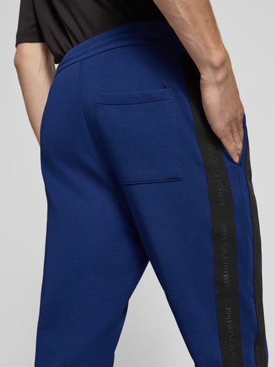 Männermodel trägt Sweatpants mit Bordüre von Armani Exchange in Blau mit schwarzer Label-Bordüre, Seitentaschen, Nahaufnahme Rückansicht. Elastischer Baumwoll-Mix und gerader Schnitt, Gesäßtasche zu sehen.