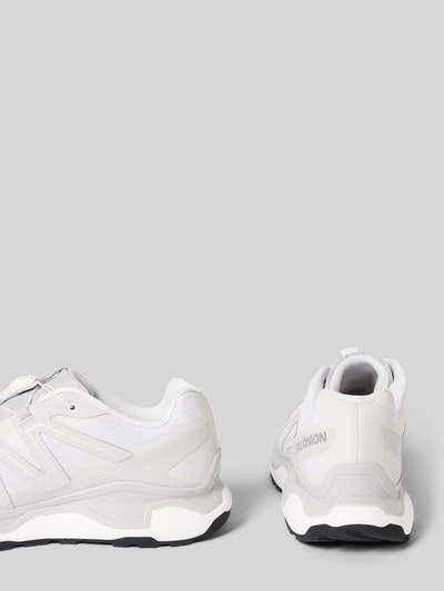 Produktfoto, Sneaker mit profilierter Sohle Modell 'XC ROAM' von Salomon, weiß-graue Farben, Logo, runde Spitze, strukturierte Textur.