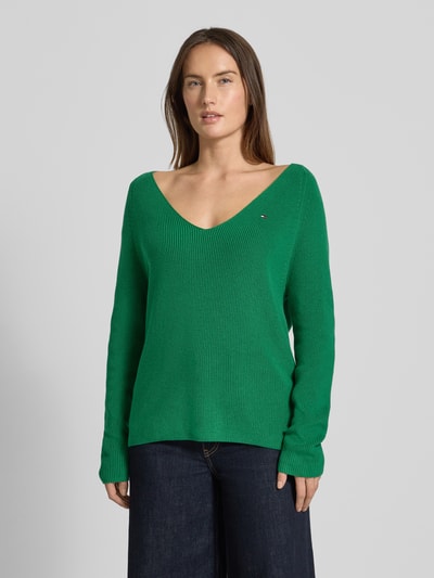 Modelka kobieca nosi Regular Fit Strickpullover aus reiner Baumwolle od Tommy Hilfiger, zielony, prążkowany, długi rękaw, dekolt V, widok całej sylwetki z przodu.