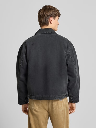 Männermodel trägt Jeansjacke mit Reißverschluss und Label-Detail Modell 'DETROIT' von Carhartt Work In Progress in Schwarz, reine Baumwolle, lockere Passform, Ganzkörperansicht Rückansicht.