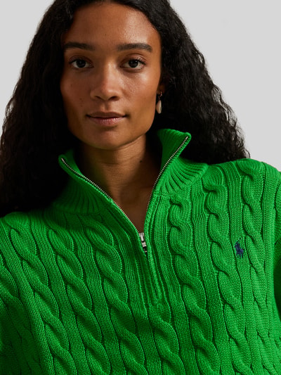 Frauenmodel trägt Troyer mit Zopfstrickmuster von Polo Ralph Lauren in Grün, Stehkragen, Logo-Stitching, Nahaufnahme Oberkörper.