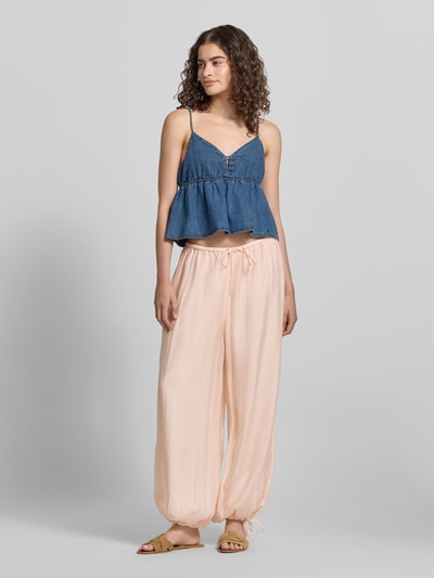 Frauenmodel trägt Relaxed Fit Stoffhose aus Viskose-Mix von Gina Tricot in zartem Rosaton, semitransparentes Design, Ganzkörperansicht von vorne. Damen Stoffhose mit elastischem Bund, Tunnelzug, eingefassten Ärmelabschlüssen, Bundweite bei Größe S: 39 cm, Innenbeinlänge: 73 cm.