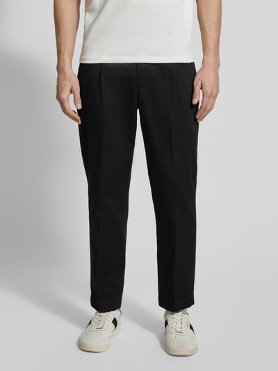 Männermodel trägt Regular Fit Chino aus Baumwoll-Mix Modell 'TAAMIR PLEATED' von Armedangels, jednokolorowy, mieszanka bawełny, wpuszczane kieszenie, kieszenie z tyłu, wyhaftowane logo, szlufki na pasek, zapięcie na haczyk i ukryty zamek błyskawiczny, efekt: jednolity kolor, krój regular fit, średni stan, Ganzkörperansicht von vorne.