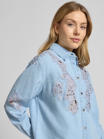 Kobiece modelka nosi Regular Fit Jeansbluse mit Stitchings od Liu Jo White z czystej bawełny, z kołnierzem koszulowym i haftem, zapięcie na guziki, długość pleców 64 cm, długość rękawa 60 cm, jasnoniebieski kolor, faktura jeansu, zbliżenie na górną część ciała, widok z przodu.