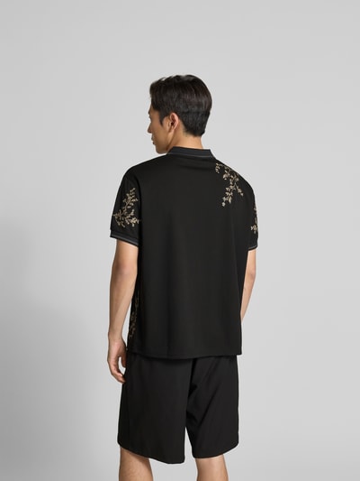 Männermodel trägt Poloshirt floralem Allover-Stitching von Don’t Waste Culture, entspannt geschnitten, schwarze Farbe, Rückansicht Ganzkörperansicht.