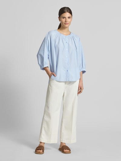 Modelka kobieca ma na sobie Regular Fit Bluse mit Raffungen Modell 'Cassy' od Soyaconcept, niebiesko-białe pasy, materiał z dodatkiem bawełny, krój regular fit, rękaw 3/4, guziki, okrągły dekolt, długość tyłu 70 cm, długość rękawa 50 cm; widok całej sylwetki z przodu.